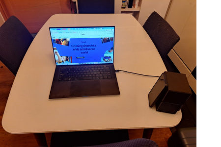 a laptop computer on a kitchen table and a cell phone propped up by two small boxes