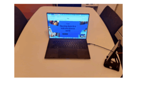 a laptop computer on a kitchen table with a phone resting on a phone holder