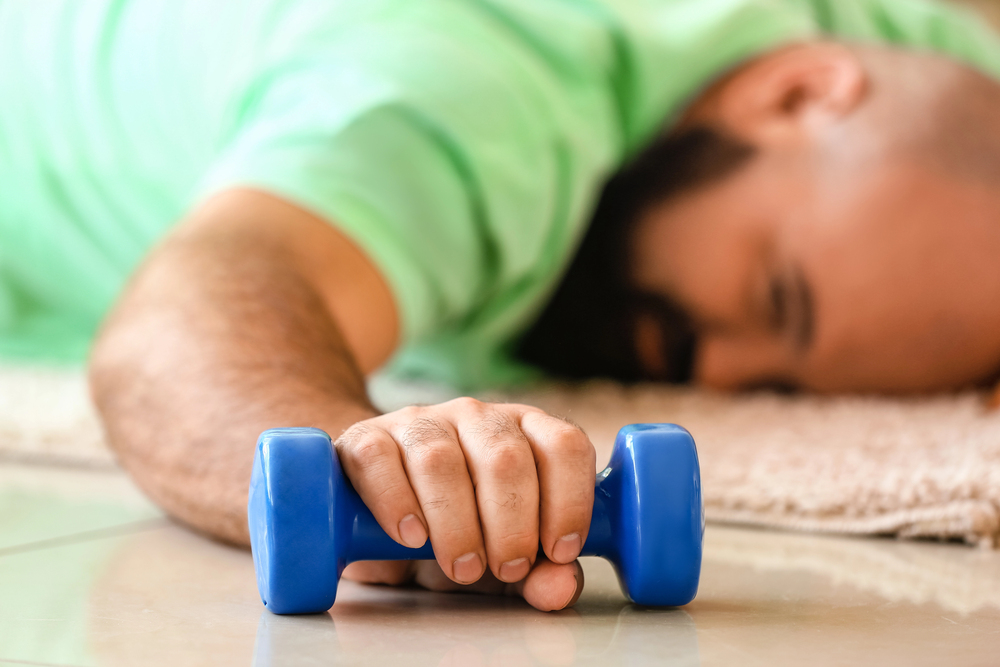 a man in a tshirt holding a weight while lying on the floor exhausted
