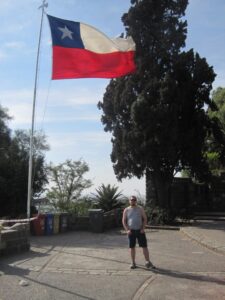 a man standing outside under a large Chilean flag flying in the wind