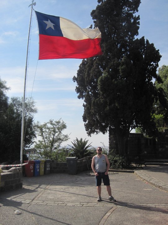 a man standing outside under a large Chilean flag flying in the wind